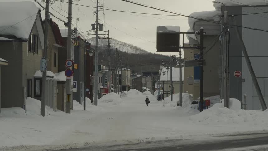 Street and a residential neighborhood covered by snow with a person walking in the background