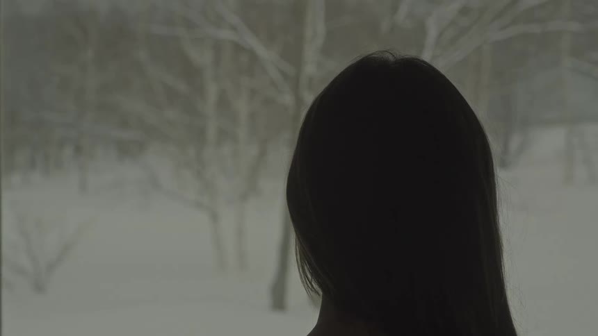 The back of the neck of a person with long hair who is looking at some dry trees with the surroundings being snowy