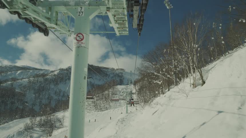 Chairlift ascending a snowy slope with skiers below and a clear blue sky above