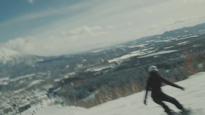 A snowboarder glides down a snowy mountain slope with a mountain in the background