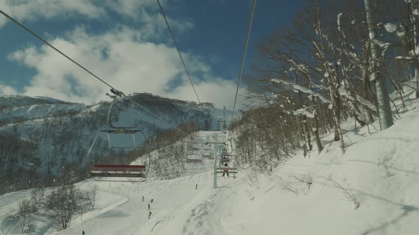 A ski lift ascends a snow covered mountain carrying skiers towards the summit under a bright blue sky