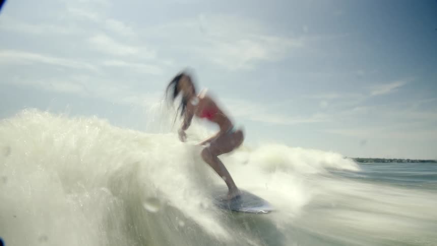 A woman is wake surfing on a sunny day