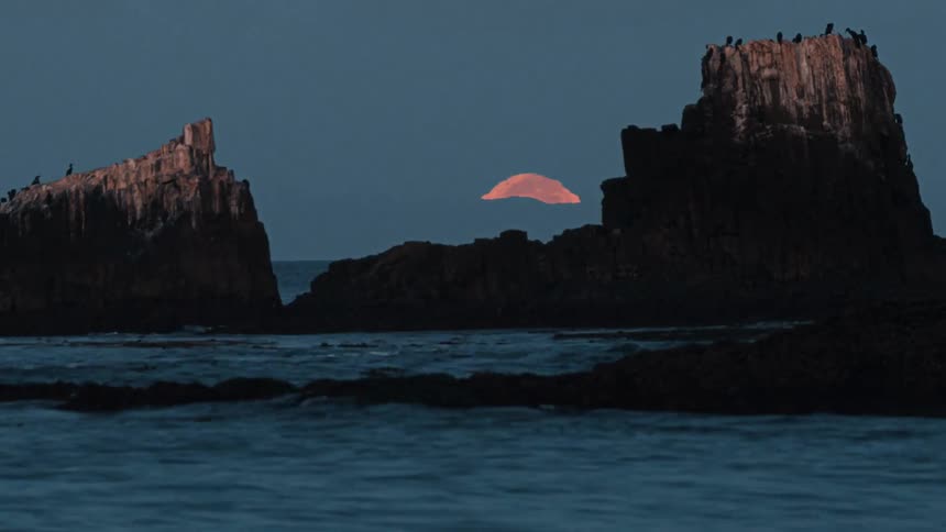 The sun sets behind the rough shore
