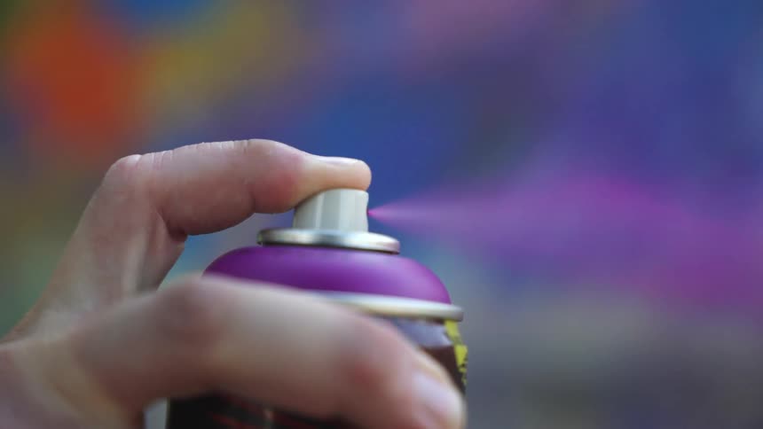A finger is pressing down on the nozzle of a purple spray paint can