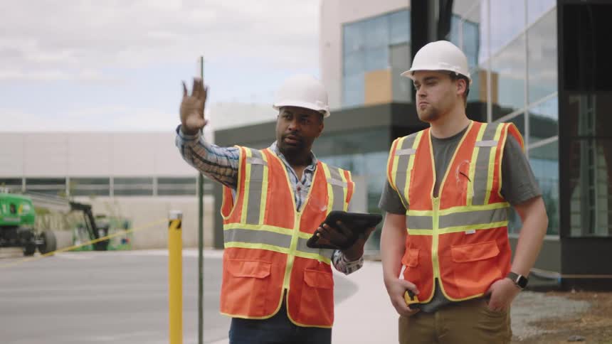 Two construction managers looking at a tablet and comparing what they see in it with a building