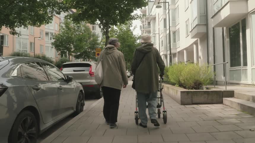 A mature couple walking down a city street one using a walker for assistance
