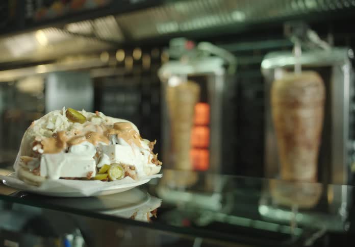 Large plate full of food on top of a glass counter with meats roasting in the background in a restaurant