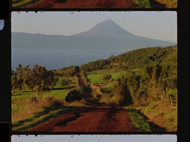 A long dirt road winding through a rural landscape with a high mountain in the distance