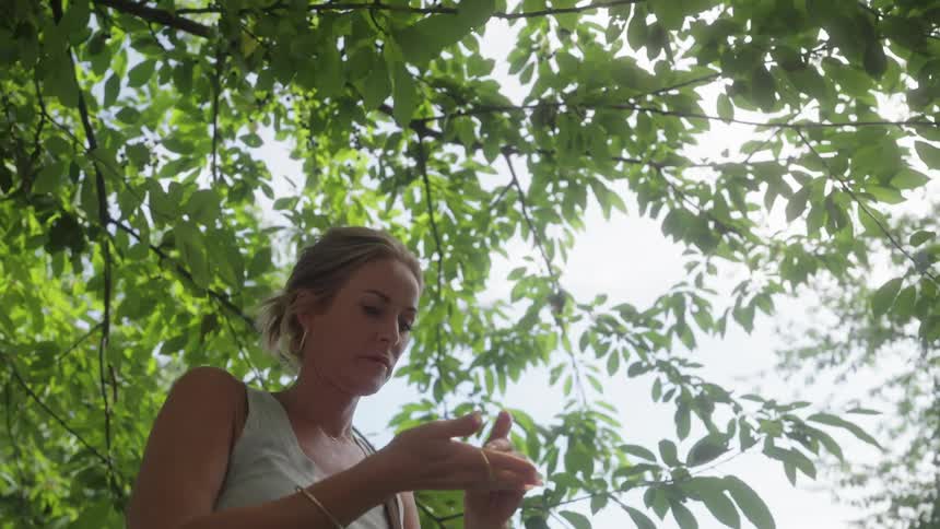 A woman pulls a tree branch to pick and eat some fruit