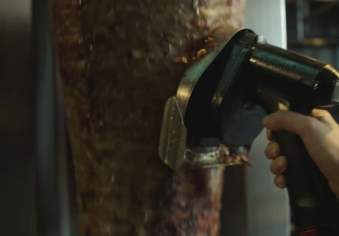 Hand holding a cutting tool and removing meat that is being roasted