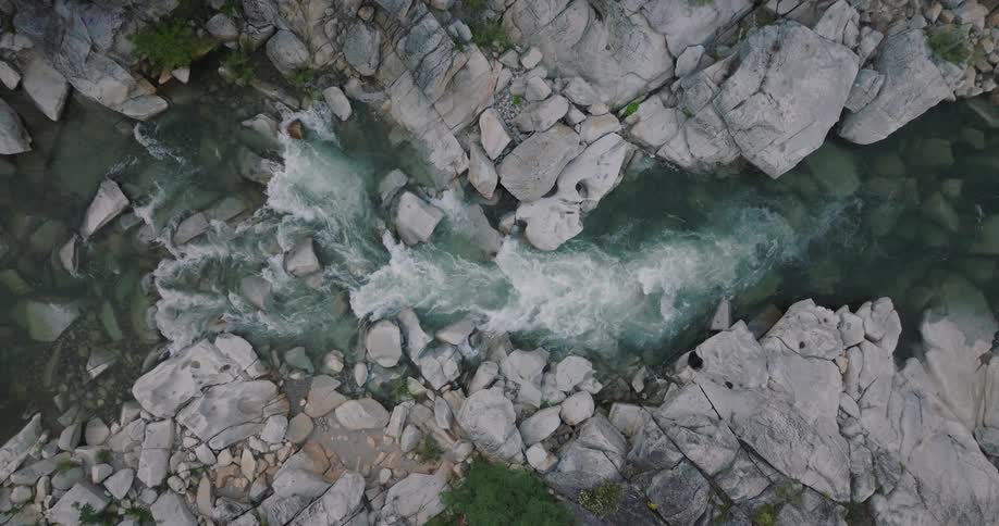 Top view of water flowing down a river surrounded by stones and rocks