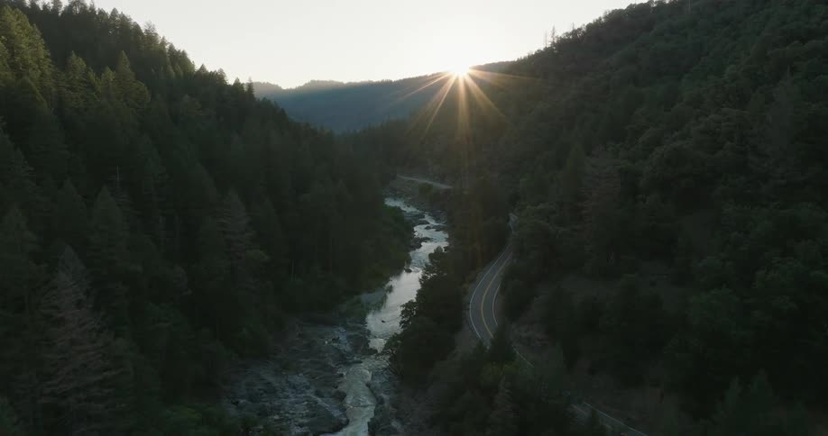 River flowing beside mountains with sun on horizon