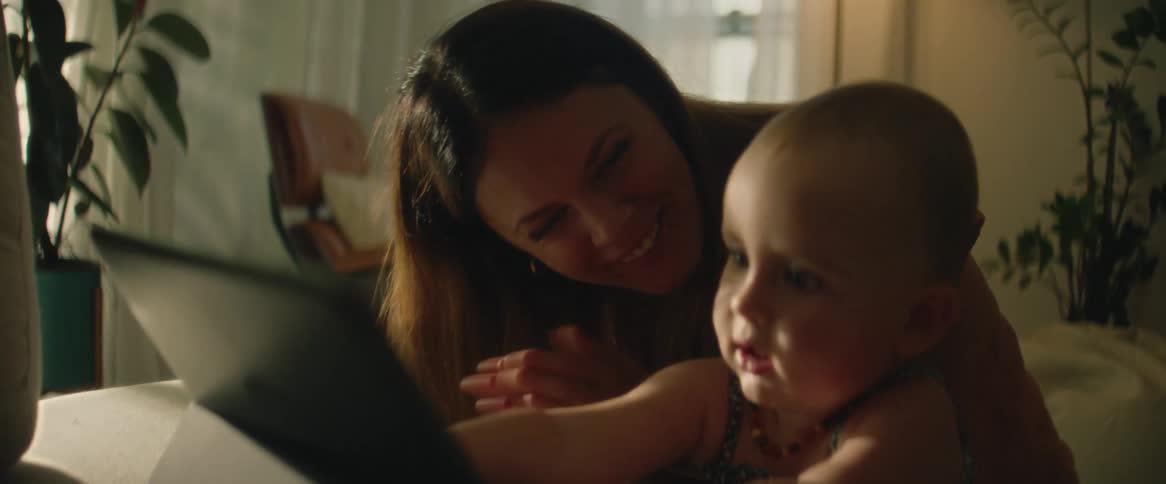 A woman clapping and laughing as a baby plays with her laptop
