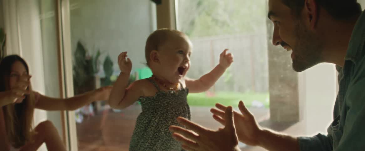 Baby daughter walking toward her father who is sitting down and he picks her up with great joy
