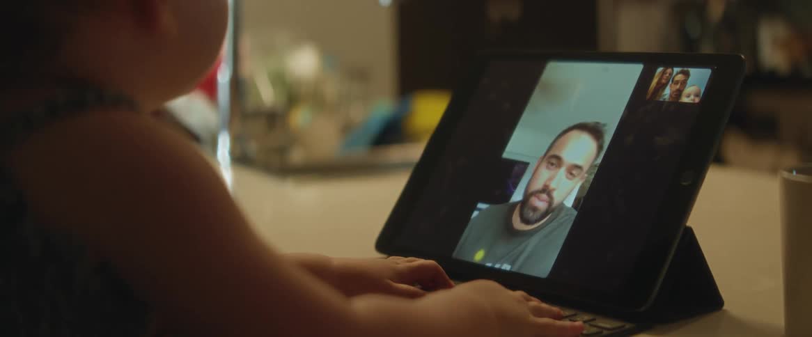 A closeup of a baby facing a tablet with other people on the screen
