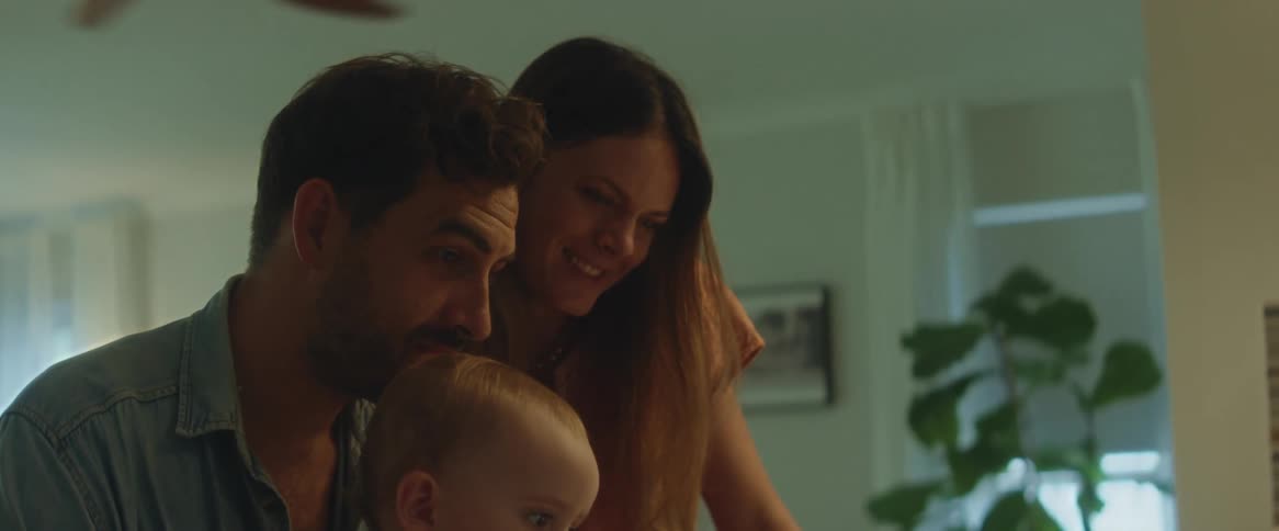 Parents watching their baby daughter as she plays with a laptop in the kitchen