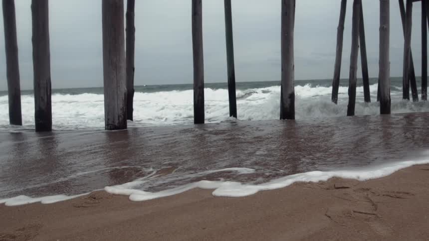 Water from the ocean rushes under a pier