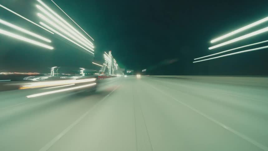 An asphalt road that passes over a bridge quickly at night and there are some cars passing on it