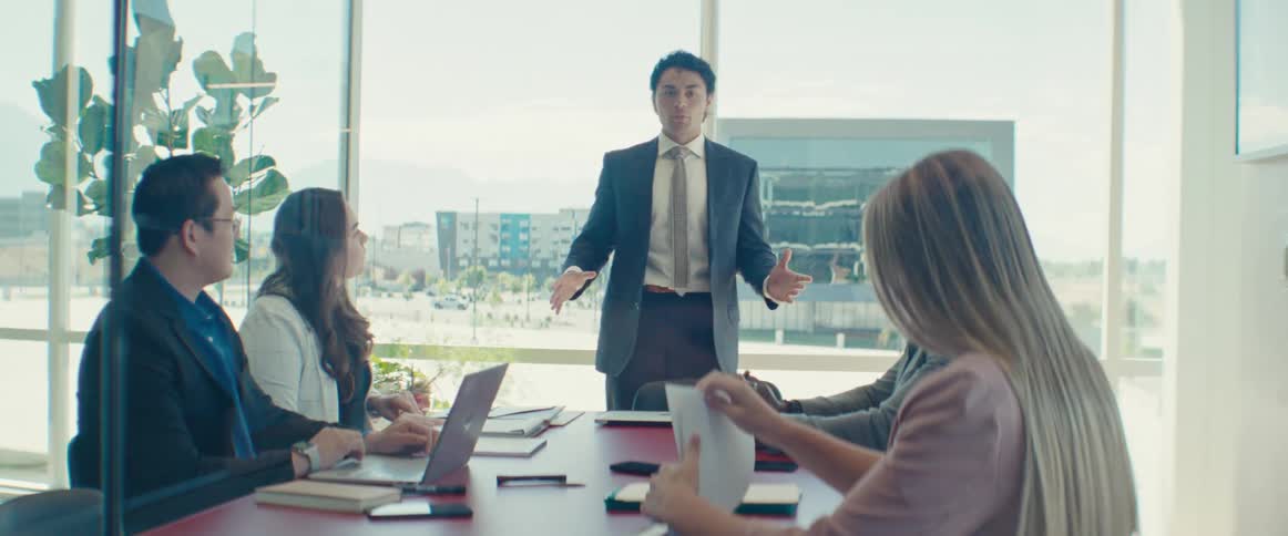 Man standing up from a table with other participants in an office meeting