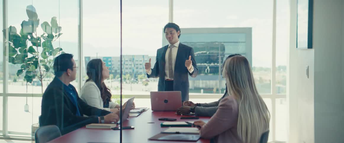 Man in suit standing in an office meeting with colleagues sitting at a table