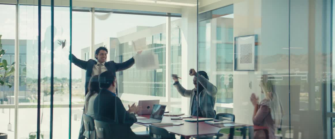 A group of workers in a meeting start celebrating by throwing papers around and clapping
