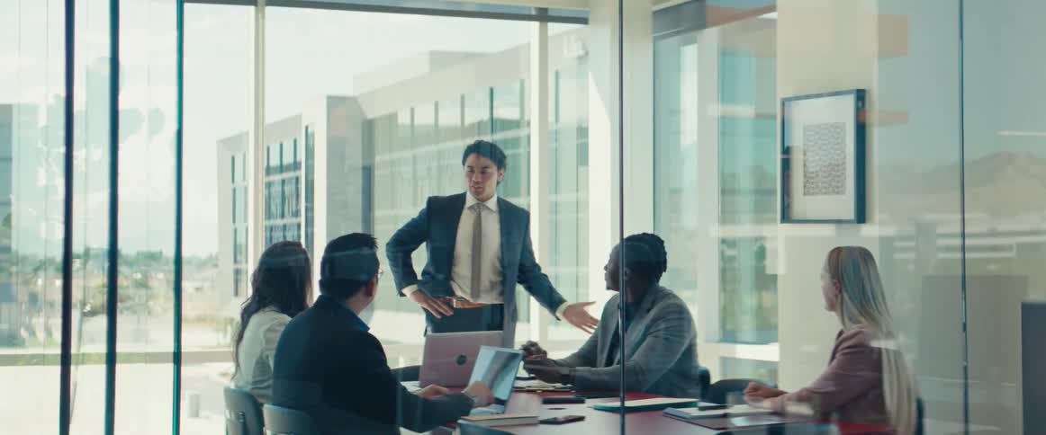Colleagues gathered around a table in a modern office with large windows in a business meeting