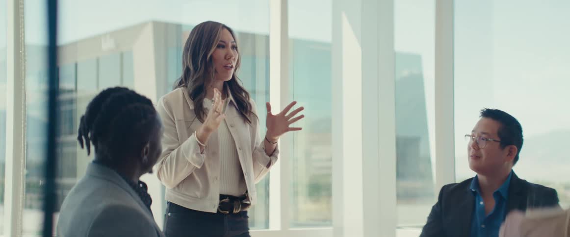 Woman standing talking to two other people sitting in an office meeting