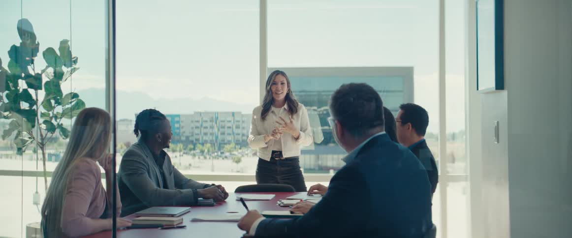 Woman stands to speak during an office meeting in a building near the outskirts