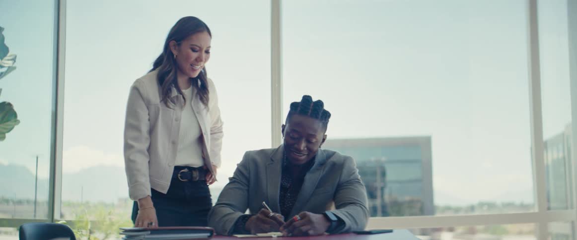 Woman pointing at a document and a man sitting writing while standing in an office environment