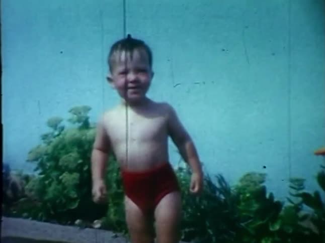 A toddler plays with a hose in the garden