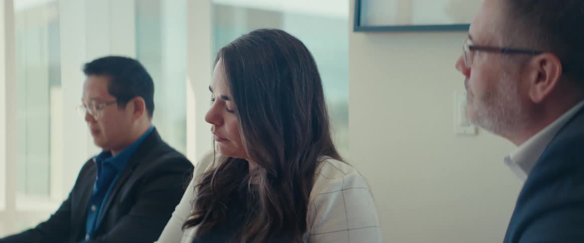Three people sit and take notes while looking to the front of the room