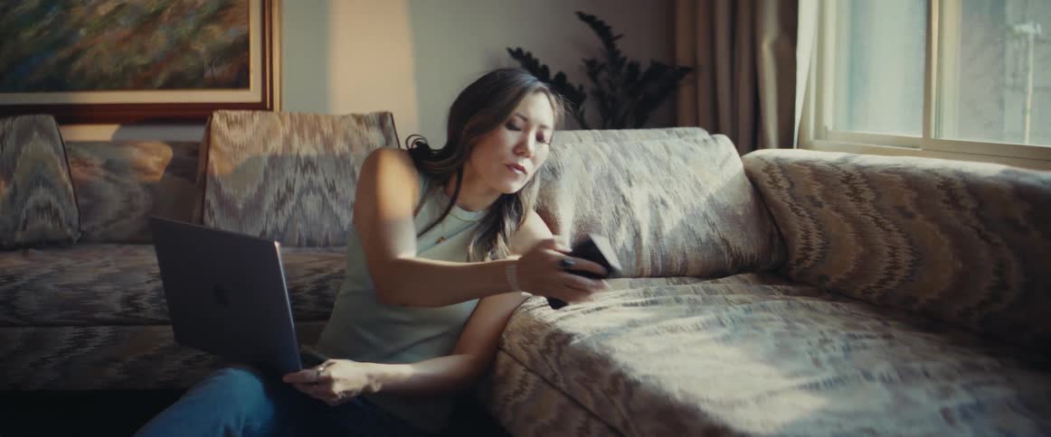 A woman on her laptop looks at her phone and hurriedly runs out of the room
