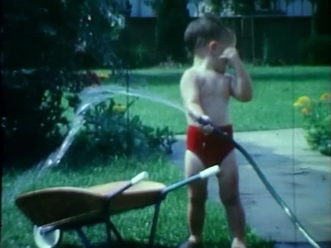 A toddler sprays himself with a hosepipe