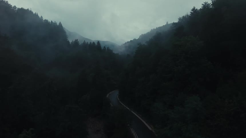 Aerial view of a highway surrounded by hills and forests on a cloudy day
