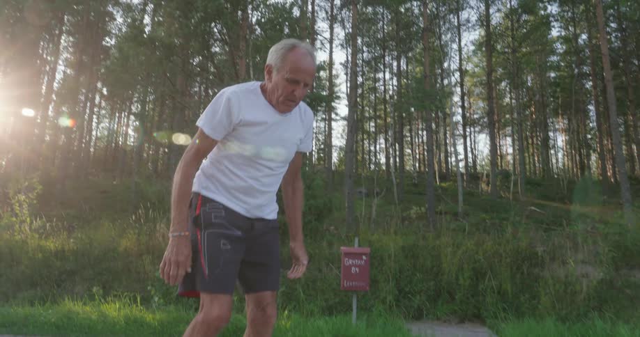 An elderly man on a parks gravel path doing warm up exercises for his legs before a run