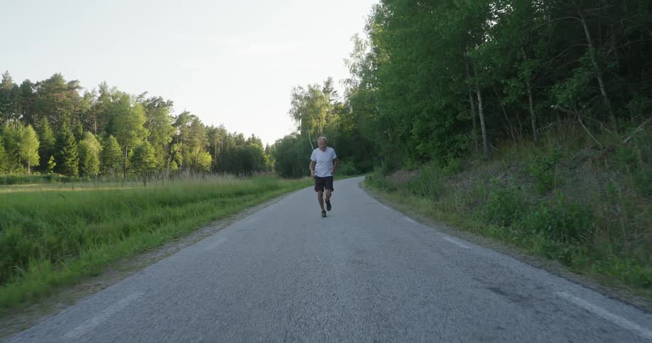 Elderly man running on a narrow paved street surrounded by vegetation