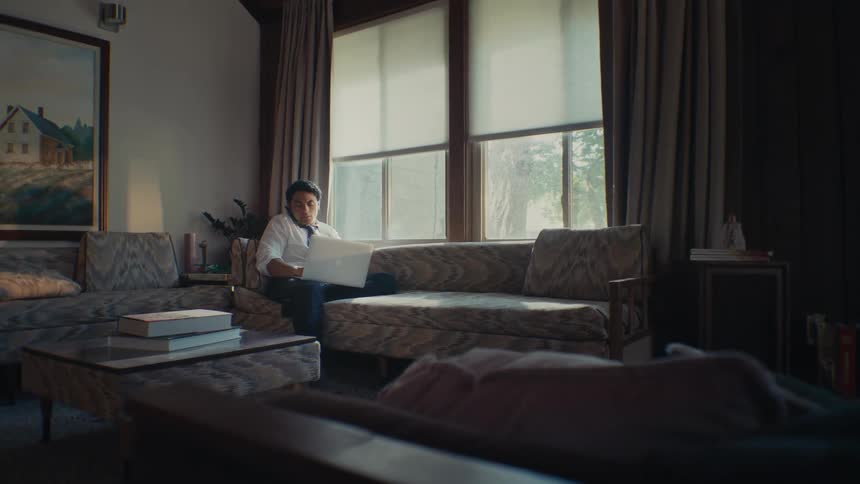 Man sitting in a living room on a phone call and typing on a laptop