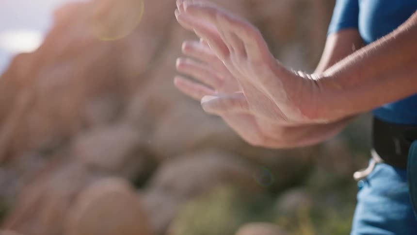 Close up of a persons hands covered in chalk as they move them around while standing outdoors near boulders