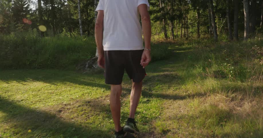 An older man walking through a forest as the sun sets behind him