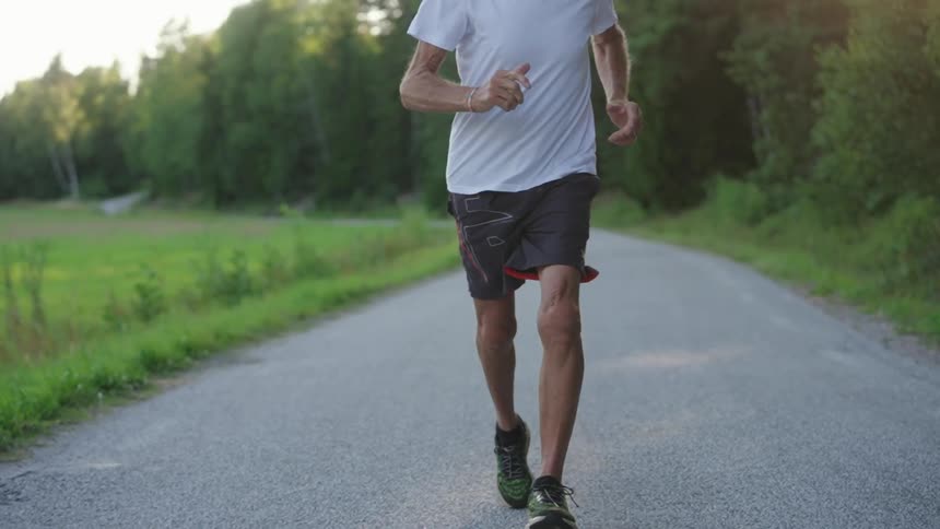 Elderly man doing cardio running on a paved road in a natural environment