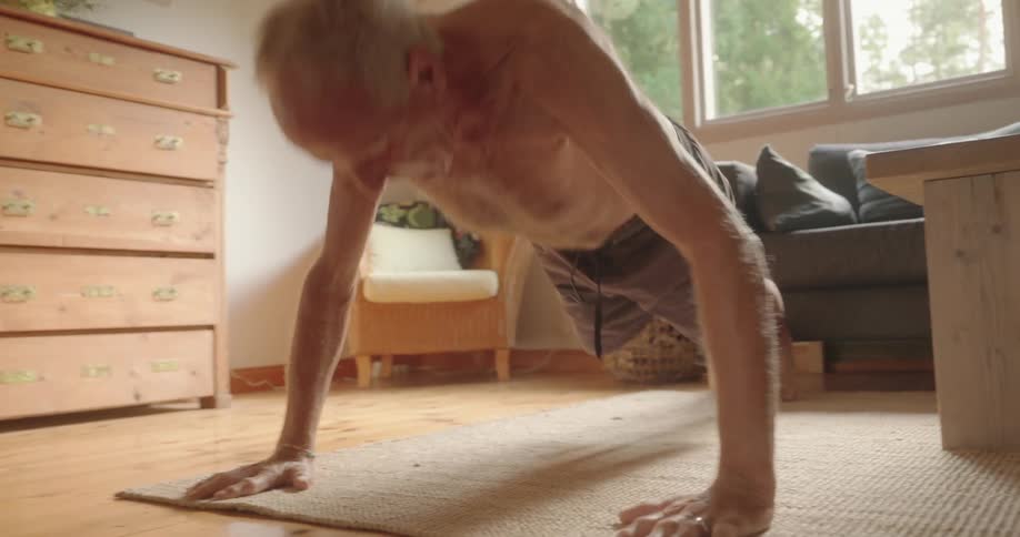 Elderly bare chested man does push ups at home in his living room