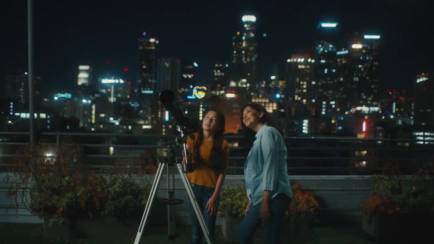 A woman looking through a telescope while another woman stands next to her as they both conversate