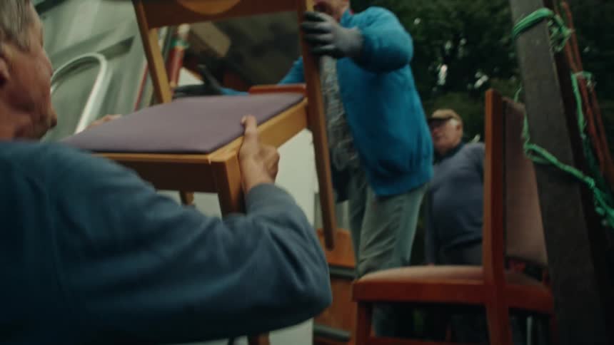 Three elderly men are putting furniture into a moving truck on a summer day