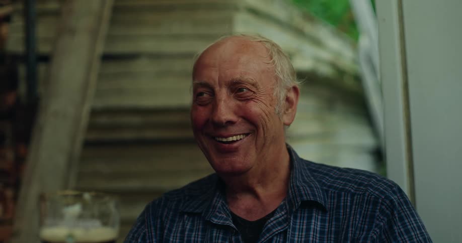 Elderly man smiles while sitting outside with a beer