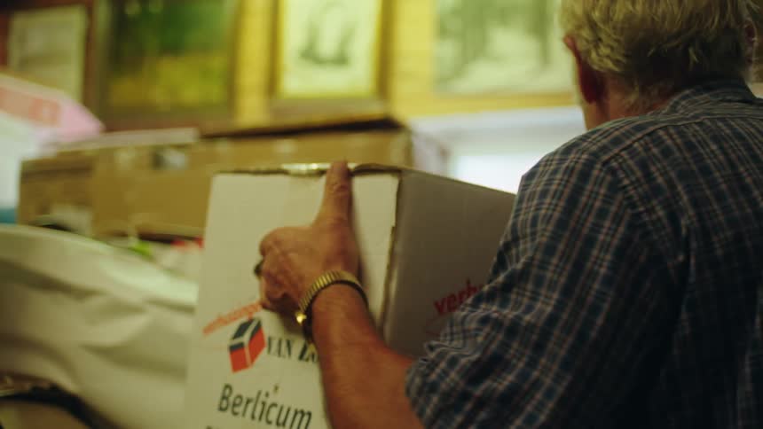 Elderly man picking up a box inside a room