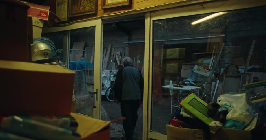 Elderly man leaving a warehouse full of rubble and old objects