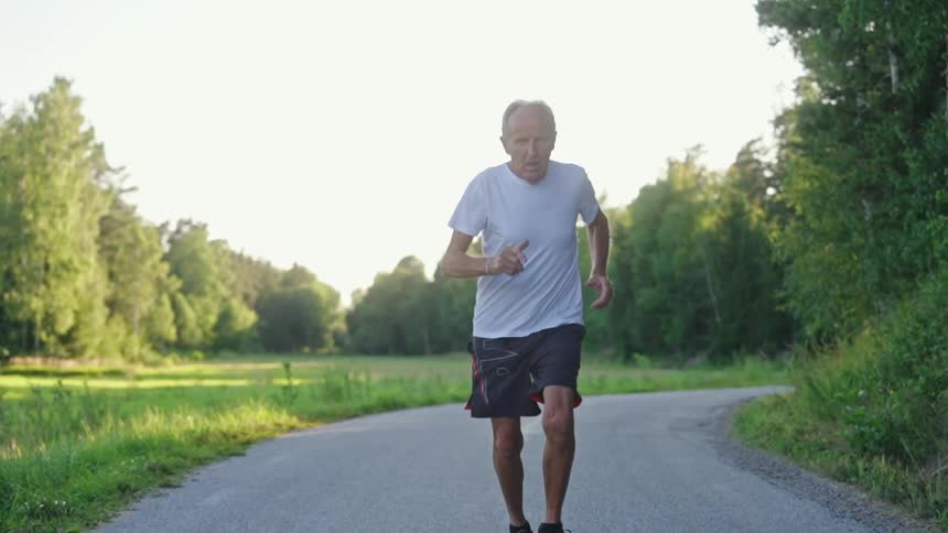 Determined elderly man running in an environment surrounded by trees