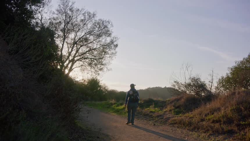 A person walking down a hiking road while overlooking nature as the sun is setting