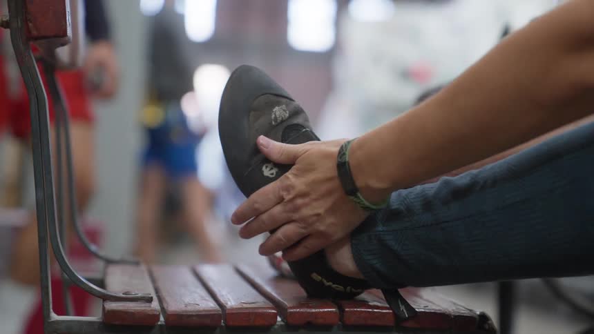 Close up of a person strapping their shoe on their foot while sitting at a table on a sidewalk