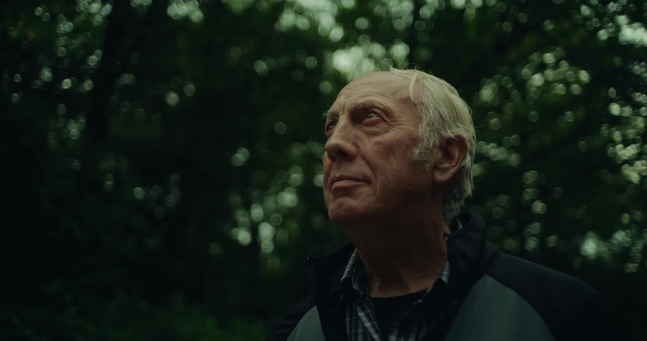 Portrait of an elderly man looking up at something with trees in the background
